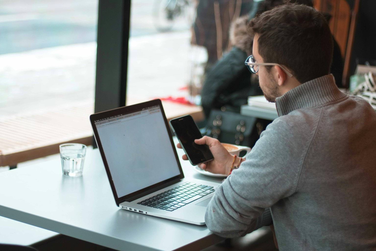 A person sitting at a table with a laptop and smartphone.