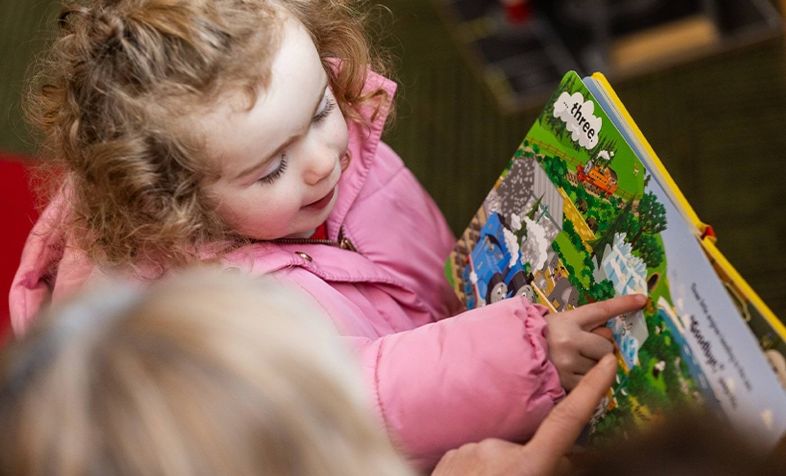 Regulatory fee increase to support regulation and child safety A child pointing on an illustration while being assisted by their educator to read a picture book